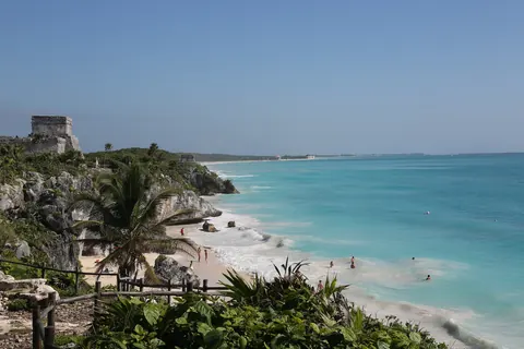 La playa frente a las ruinas de Tulum: el templo de El Castillo sobre el acantilado, palmeras y el mar turquesa del Caribe mexicano
