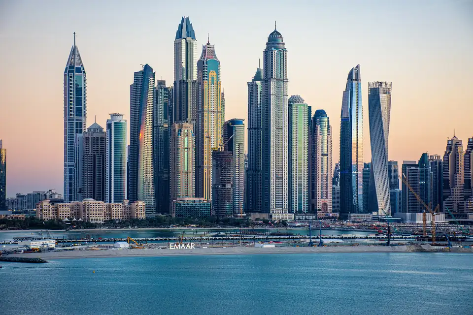 Los rascacielos de Dubai Marina se recortan contra un cielo de atardecer, con la costa y el mar en primer plano