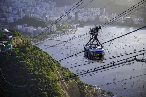Una cabina del teleférico del Pan de Azúcar cruza sobre la bahía de Botafogo, con veleros anclados y los edificios de Río de Janeiro detrás