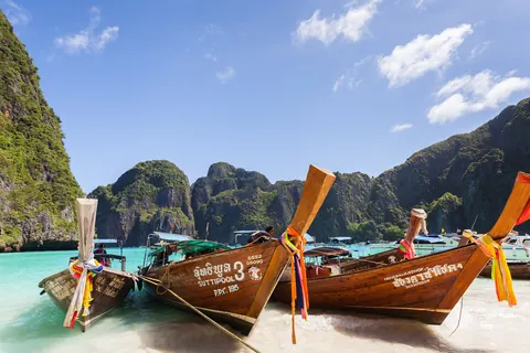 Botes long-tail de madera amarrados en la playa Maya, en Ko Phi Phi, Tailandia, con acantilados de piedra caliza y agua turquesa de fondo